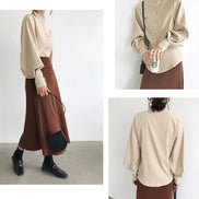 Person wearing a beige blouse and brown skirt with a black handbag on a white background