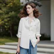 Woman wearing a white shirt with rolled-up sleeves and blue jeans on a plain background