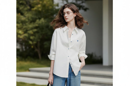 Woman wearing a white shirt with rolled-up sleeves and blue jeans on a plain background