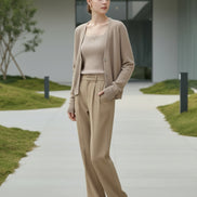 A person wearing a fuzzy beige cardigan over a ribbed mauve top and tan pants, standing indoors 