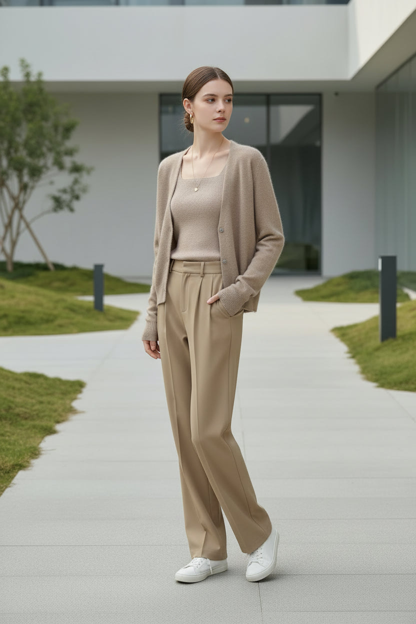 A person wearing a fuzzy beige cardigan over a ribbed mauve top and tan pants, standing indoors 