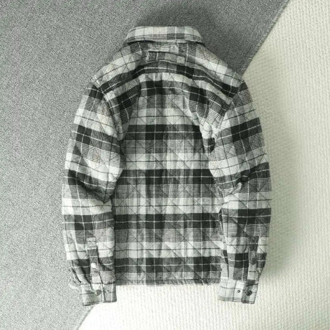 A black and white plaid flannel shirt jacket shown from the back, laid flat on a textured gray surface.