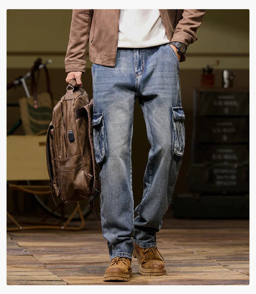 Front view of a model wearing faded blue cargo pants with large flap thigh pockets and straight legs, holding a brown backpack and wearing brown boots.