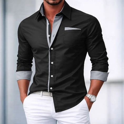 Man wearing a navy button-up shirt with light gray trim and white pants against a blurred background