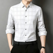 A man wearing a white long-sleeve button-up shirt with a black grid plaid pattern, paired with black trousers and a black belt