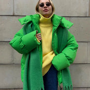 Person wearing a bright green coat with a yellow sweater and blue jeans against a stone wall.