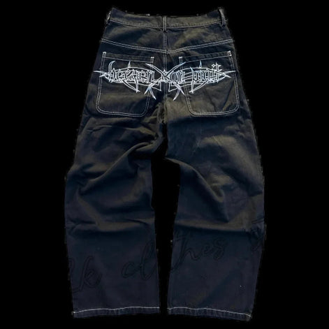 Back view of black wide-leg jeans laid flat, featuring white contrast stitching and a large white gothic lettering graphic across both back pockets.