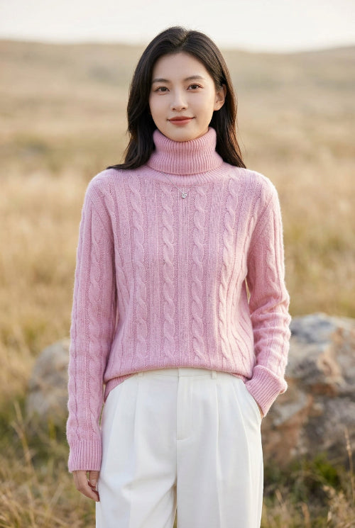 A person wearing a pink cable-knit sweater, holding a phone to take a mirror selfie in a brightly lit indoor setting.
