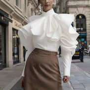 Person wearing a white blouse with ruffled details and a brown skirt on a city street.