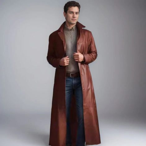 Man wearing a long brown leather coat over a sweater and jeans on a gray background
