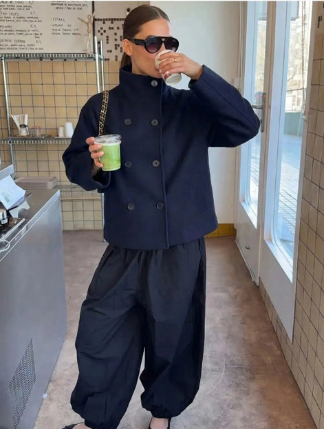 Woman wearing a navy stand-collar short coat while holding drinks in a café