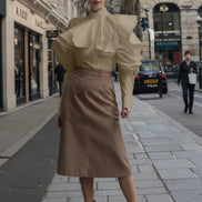 Person wearing a beige blouse with ruffled sleeves on a city street.