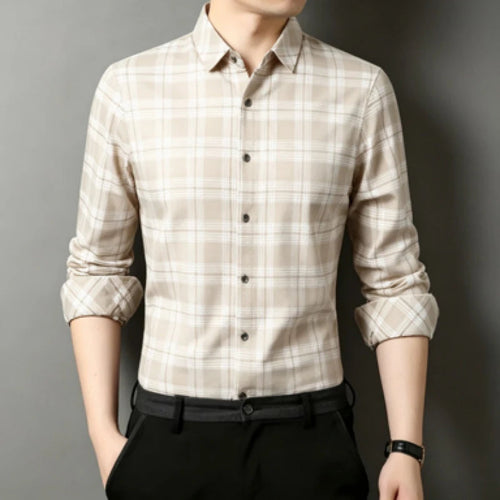 A man wearing a beige and white plaid long-sleeve button-down shirt with black trousers, shown from the neck down against a dark gray background.