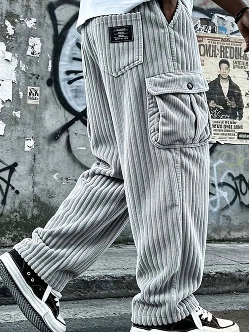 A person wearing light gray ribbed corduroy cargo pants with large front flap pockets, shown from the waist down in an urban street setting 