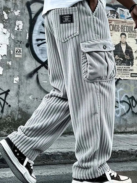 A person wearing light gray ribbed corduroy cargo pants with large front flap pockets, shown from the waist down in an urban street setting 