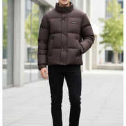 A dark brown puffer jacket with a high stand-up collar and front button closure, displayed on a hanger in a retail store setting.
