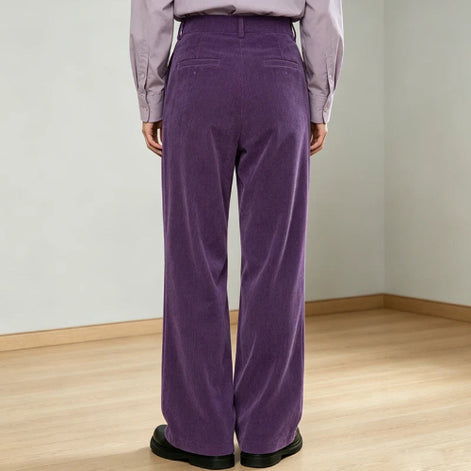 A person shown from the back wearing high-waisted, wide-leg purple corduroy trousers with a light purple shirt and black shoes, 