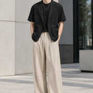 A men's two-piece outfit set featuring a black short-sleeve blazer layered over a black t-shirt, paired with high-waisted beige wide-leg trousers, 