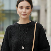A person wearing a black cable-knit sweater, styled with a silver pendant 