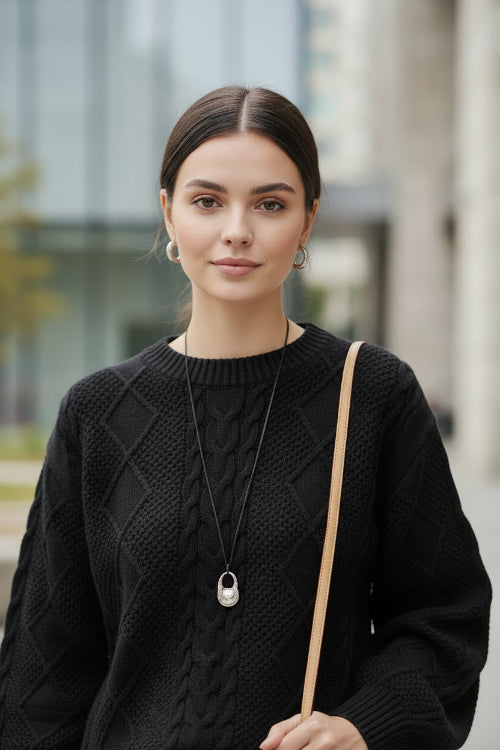 A person wearing a black cable-knit sweater, styled with a silver pendant 
