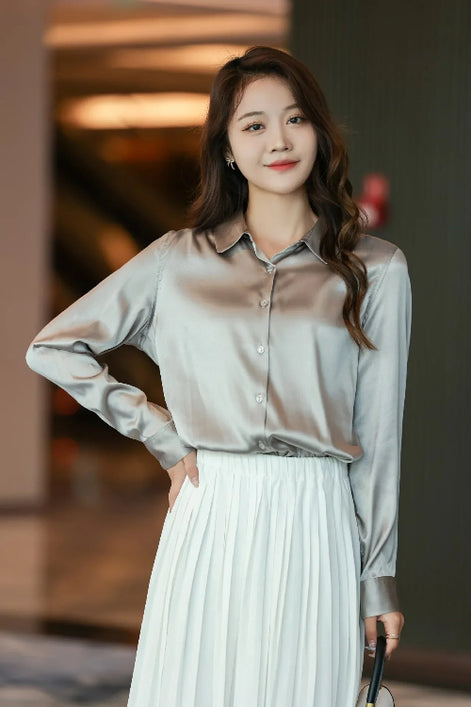 Silver gray silk shirt worn by a model with a white pleated skirt indoors.