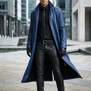 Man wearing a long blue coat over a black outfit on a white background