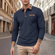 Man wearing a navy long-sleeve polo shirt with plaid accents on a city street.