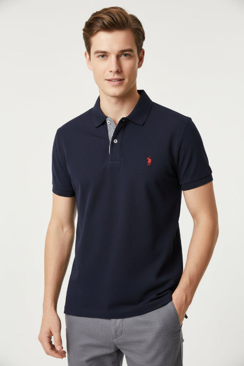 Navy blue polo shirt with a red logo being held by a hand, with other shirts in the background.