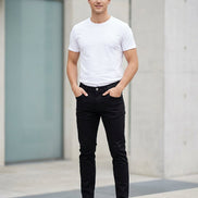 Black slim-fit jeans hanging on a wooden hanger against a textured gray wall.