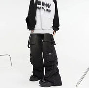 Model wearing washed black baggy cargo jeans with multiple flap pockets and hanging side straps, paired with a black-and-white top and chunky black shoes.