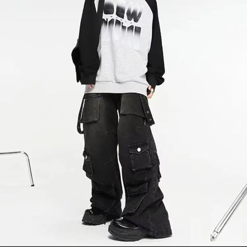 Model wearing washed black baggy cargo jeans with multiple flap pockets and hanging side straps, paired with a black-and-white top and chunky black shoes.