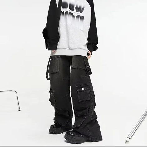 Model wearing washed black baggy cargo jeans with multiple flap pockets and hanging side straps, paired with a black-and-white top and chunky black shoes.
