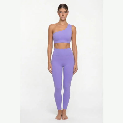 Woman wearing a purple one-shoulder top and leggings on a white background