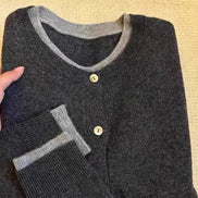 Folded dark gray sweater with light gray trim on a beige surface