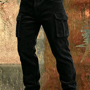 Black corduroy cargo pants with a brown leather belt, shown from the waist down against a textured, rustic brown and orange background.