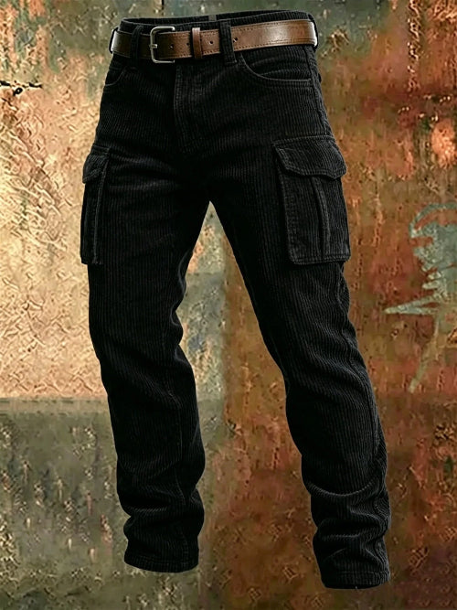 Black corduroy cargo pants with flap thigh pockets and a brown belt against a textured rust-colored metal background.