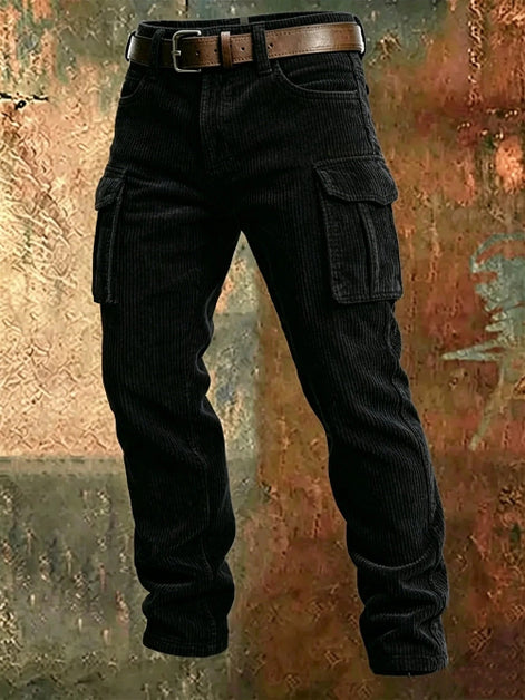 Black corduroy cargo pants with flap thigh pockets and a brown belt against a textured rust-colored metal background.