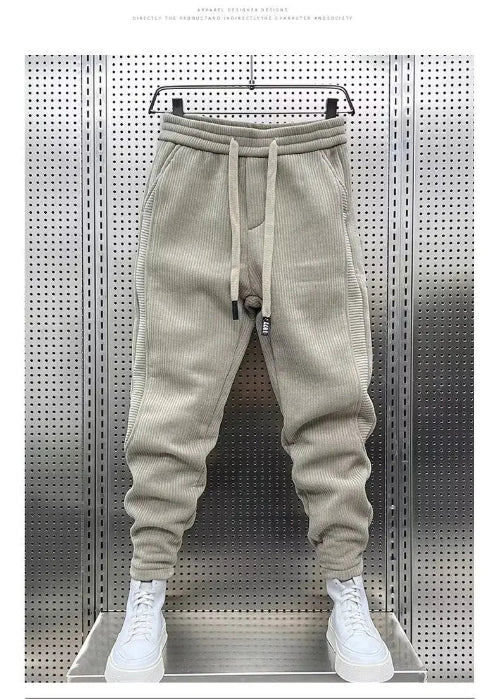 Beige baggy sweatpants hanging on a hanger against a perforated metal wall, with white sneakers below and a white border around the photo.