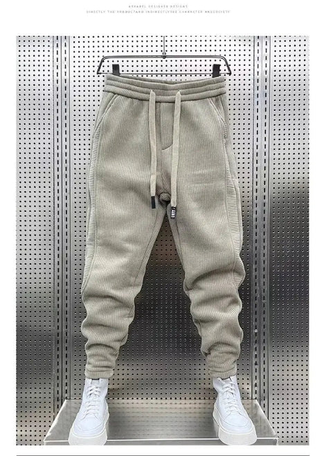 Beige baggy sweatpants hanging on a hanger against a perforated metal wall, with white sneakers below and a white border around the photo.