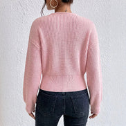 A woman shown from the back wearing a light pink ribbed knit sweater and dark blue jeans against a textured white wall.