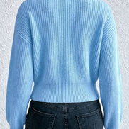A person shown from the back wearing a light blue ribbed knit sweater and dark blue jeans against a white textured wall.