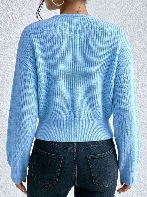 A person shown from the back wearing a light blue ribbed knit sweater and dark blue jeans against a white textured wall.