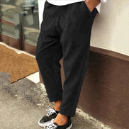 Person wearing black pants and black sneakers leaning against a wall.