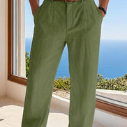 Person wearing green pants with a brown belt, standing by a window with a view of the ocean.