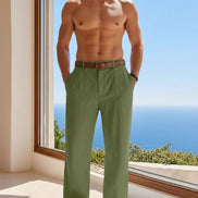 Person wearing green pants with a brown belt, standing by a window with a view of the ocean.