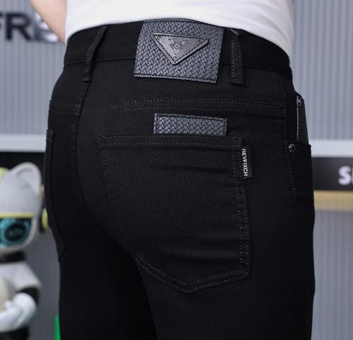Close-up rear view of a person wearing black jeans with a textured triangular patch on the back waistband and a small vertical brand tab 