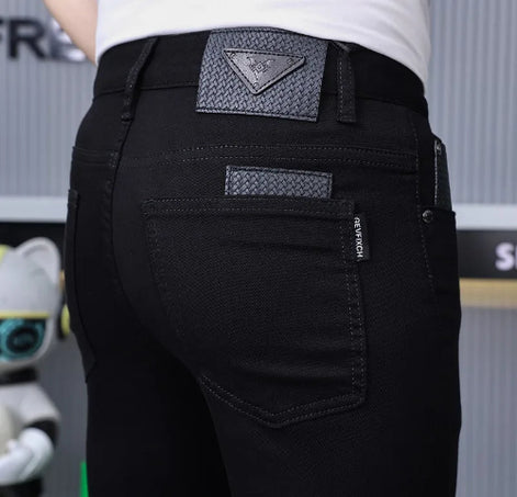 Close-up rear view of a person wearing black jeans with a textured triangular patch on the back waistband and a small vertical brand tab 