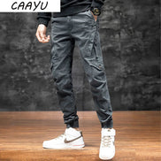 Front view of a model wearing gray cargo pants with angled thigh pockets and gathered ankle cuffs, paired with white high-top sneakers against a dark wall.