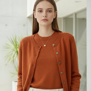 Person wearing an orange cardigan over a white shirt and black pants, standing against a neutral background.