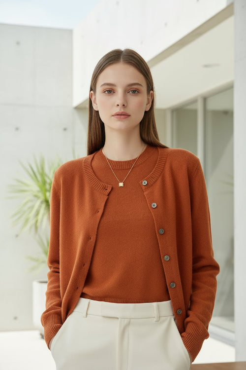 Person wearing an orange cardigan over a white shirt and black pants, standing against a neutral background.